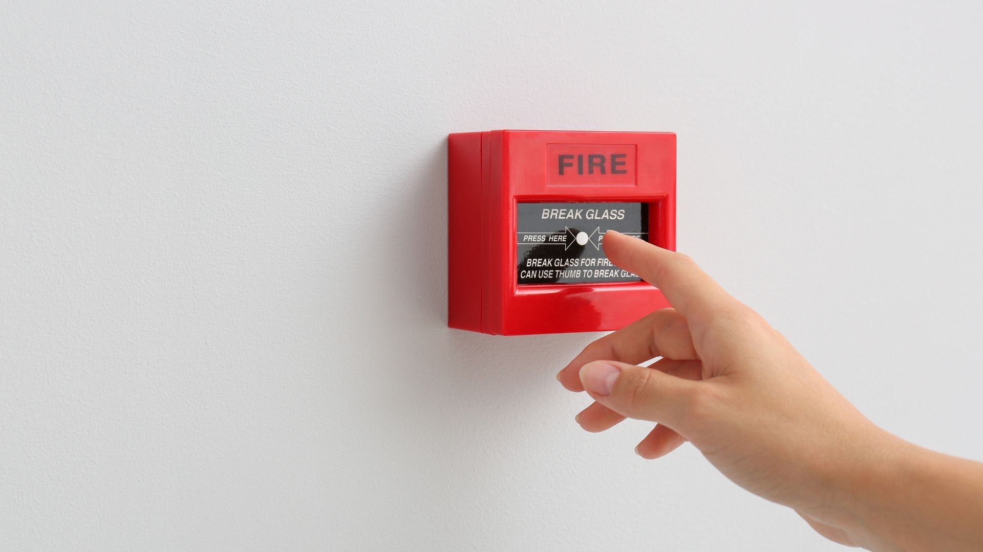 Pulsante di allarme rosso montato su una parete e premuto da una persona